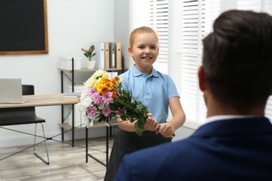 Photo of Schoolgirl with bouquet congratulating her pedagogue in classroom. Teacher's day