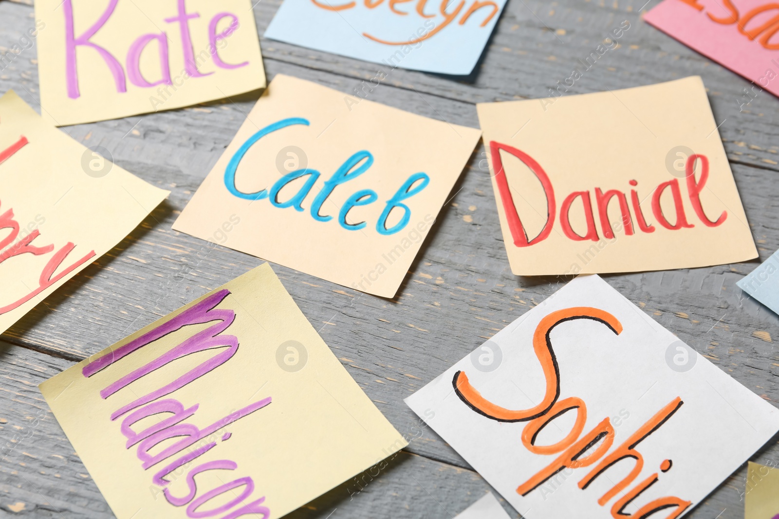 Photo of Colorful paper sheets with written different baby names on grey wooden table, closeup