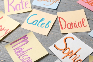 Colorful paper sheets with written different baby names on grey wooden table, closeup