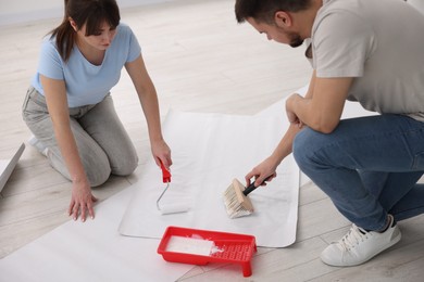 Couple applying glue onto wallpaper sheet in room