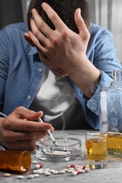 Photo of Alcohol and drug addiction. Man with smoldering cigarettes, whiskey and pills at grey textured table