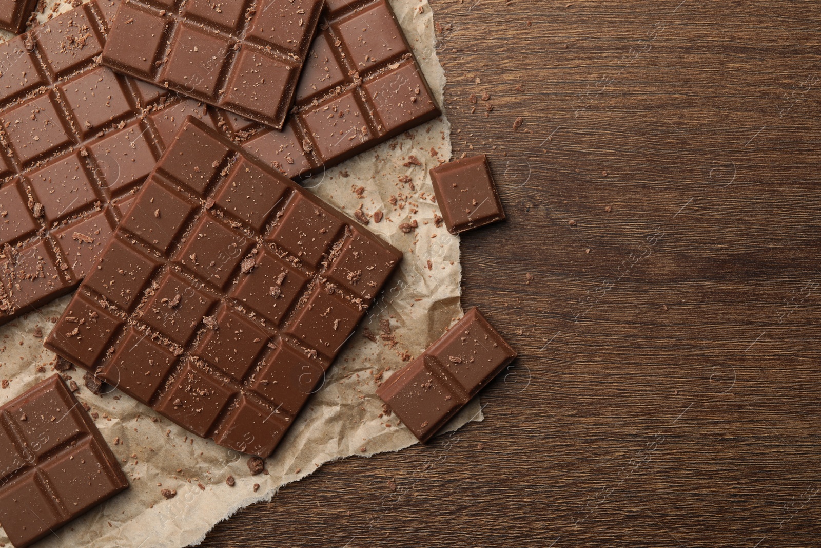 Photo of Pieces and crumbs of tasty chocolate bars on wooden table, top view. Space for text