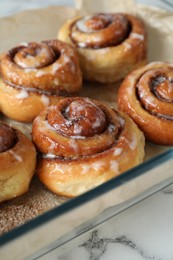 Baking dish with tasty cinnamon rolls on white marble table, closeup