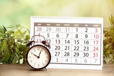 Calendar and alarm clock on wooden table against blurred green background