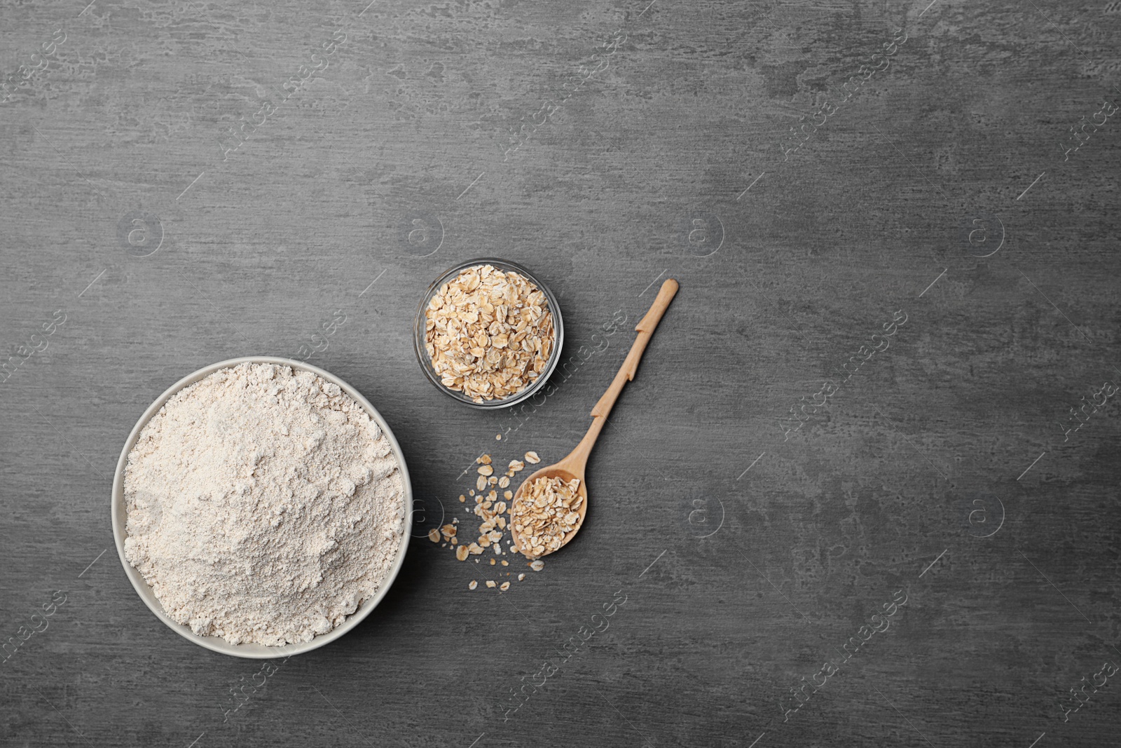 Photo of Bowl with oat flour and flakes in spoon on gray background