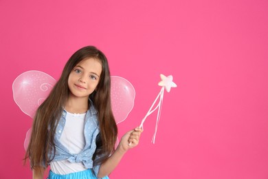 Photo of Cute little girl in fairy costume with wings and magic wand on pink background. Space for text