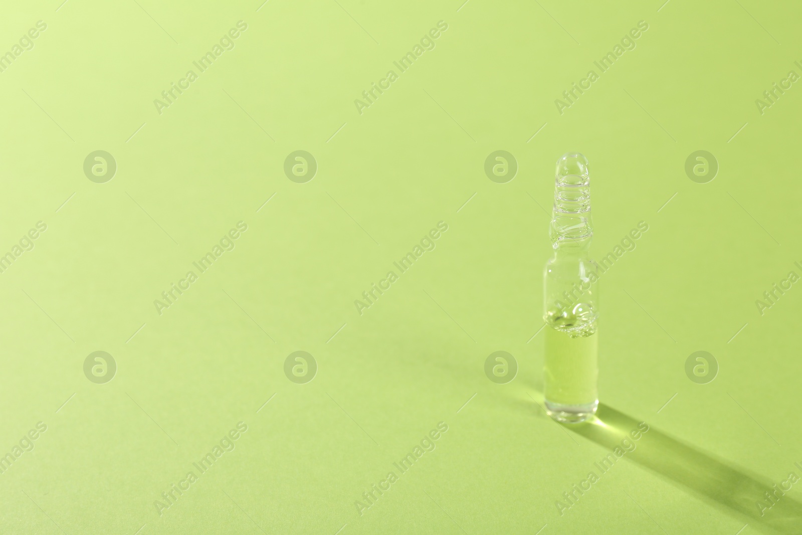 Photo of Glass ampoule with liquid on light green background. Space for text