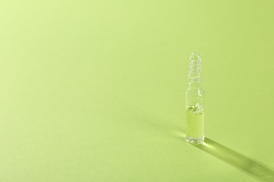 Photo of Glass ampoule with liquid on light green background. Space for text