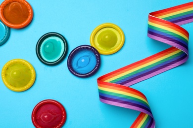 Colorful condoms and rainbow ribbon on light blue background, flat lay. LGBT concept