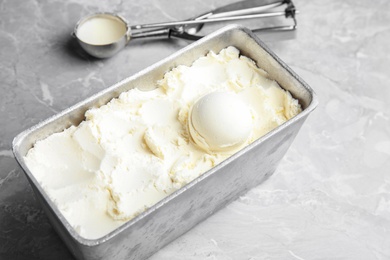Photo of Container with delicious vanilla ice cream and scoop on table