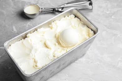 Container with delicious vanilla ice cream and scoop on table