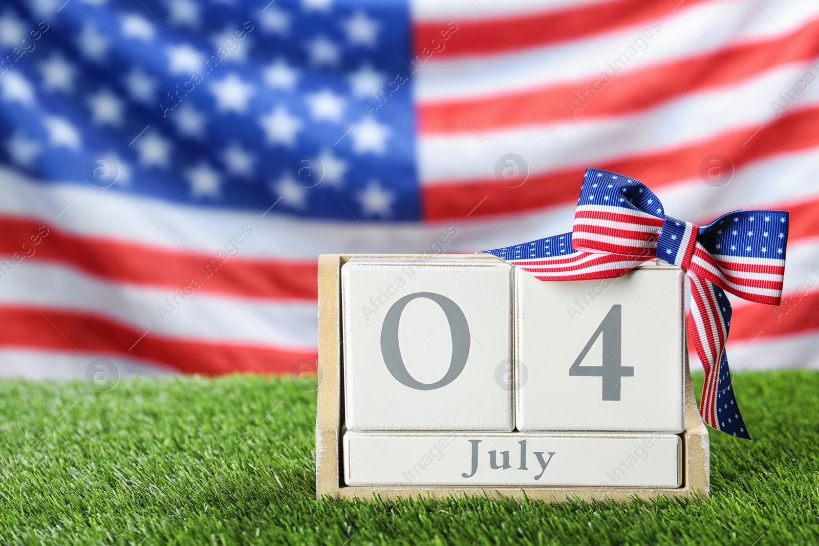 Photo of Wooden calendar with bow on green grass against USA flag, space for text. Happy Independence Day