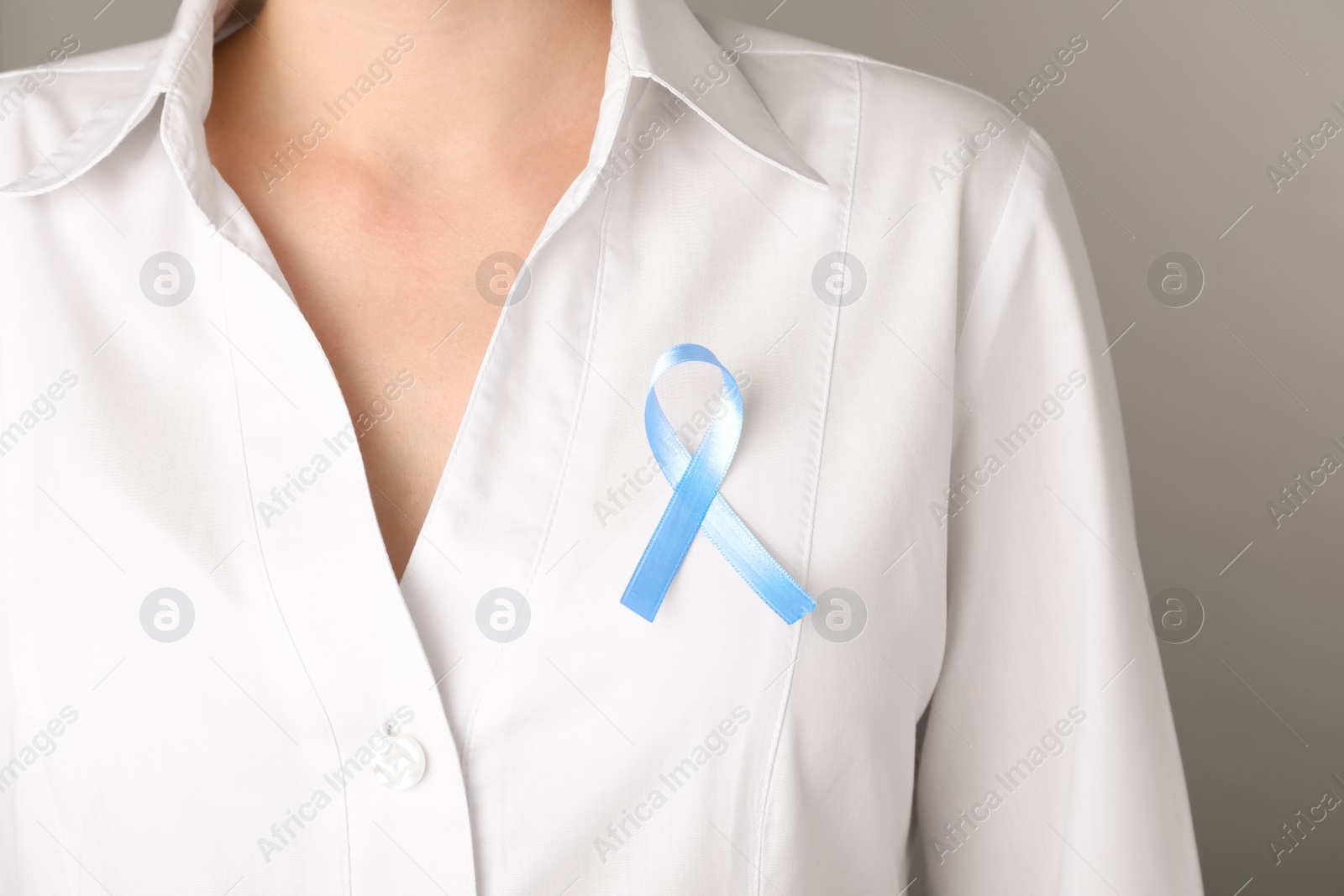 Photo of Woman with light blue awareness ribbon on grey background, closeup