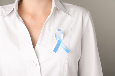 Woman with light blue awareness ribbon on grey background, closeup