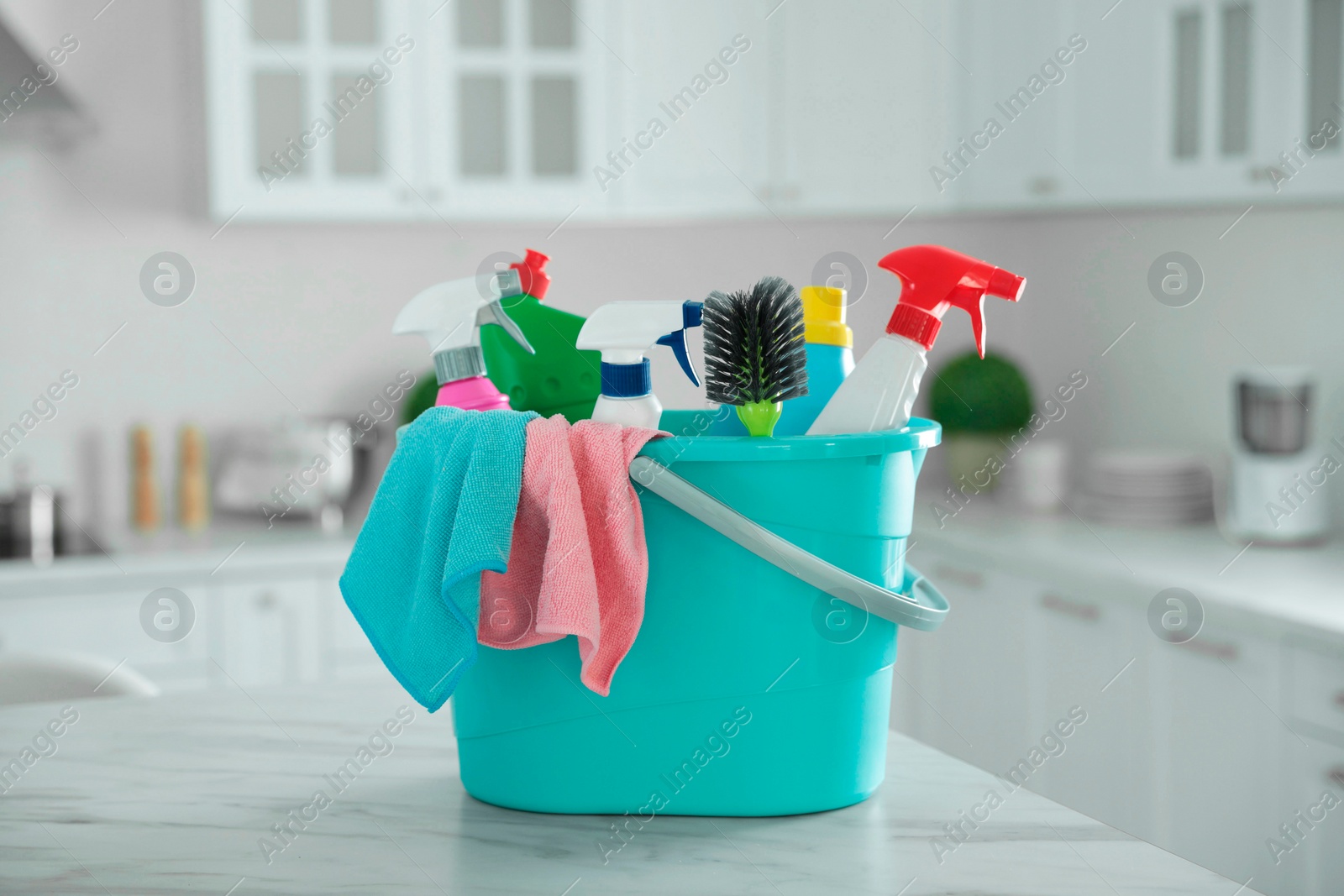 Photo of Plastic bucket with different cleaning supplies on table in kitchen