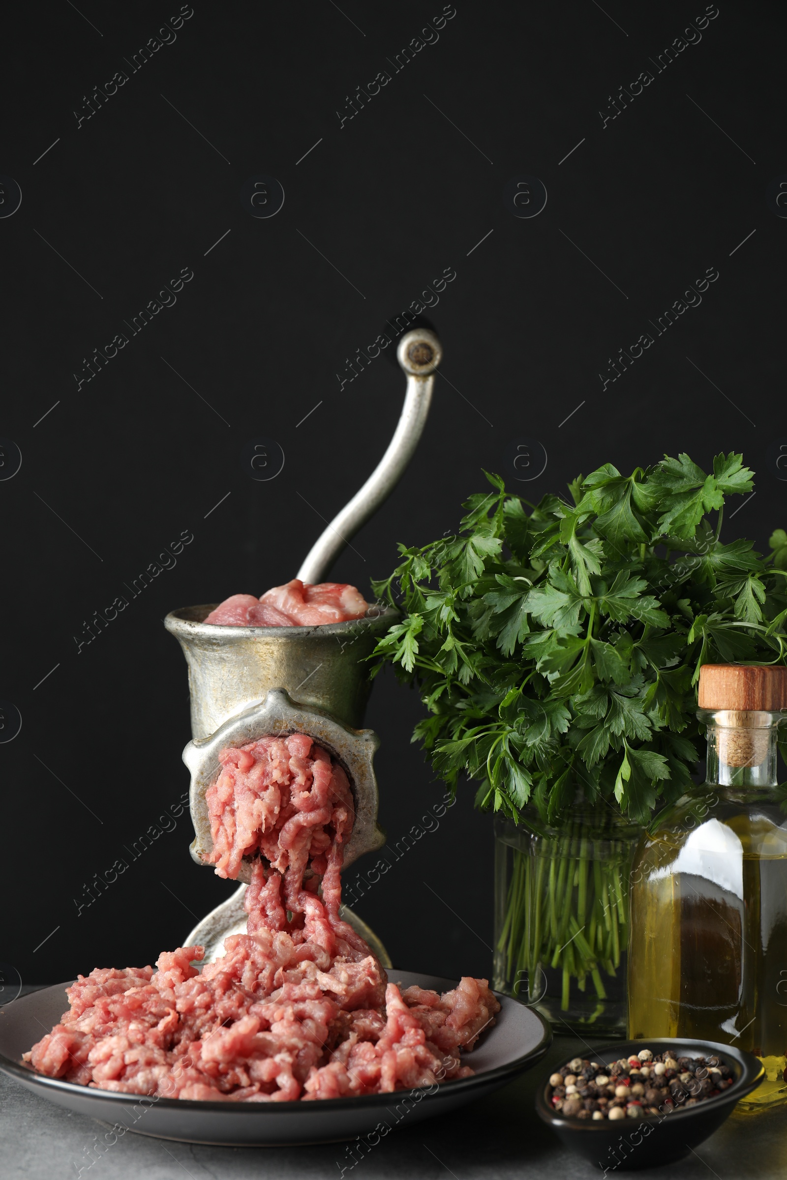 Photo of Manual meat grinder with beef mince, spices, oil and parsley on grey table