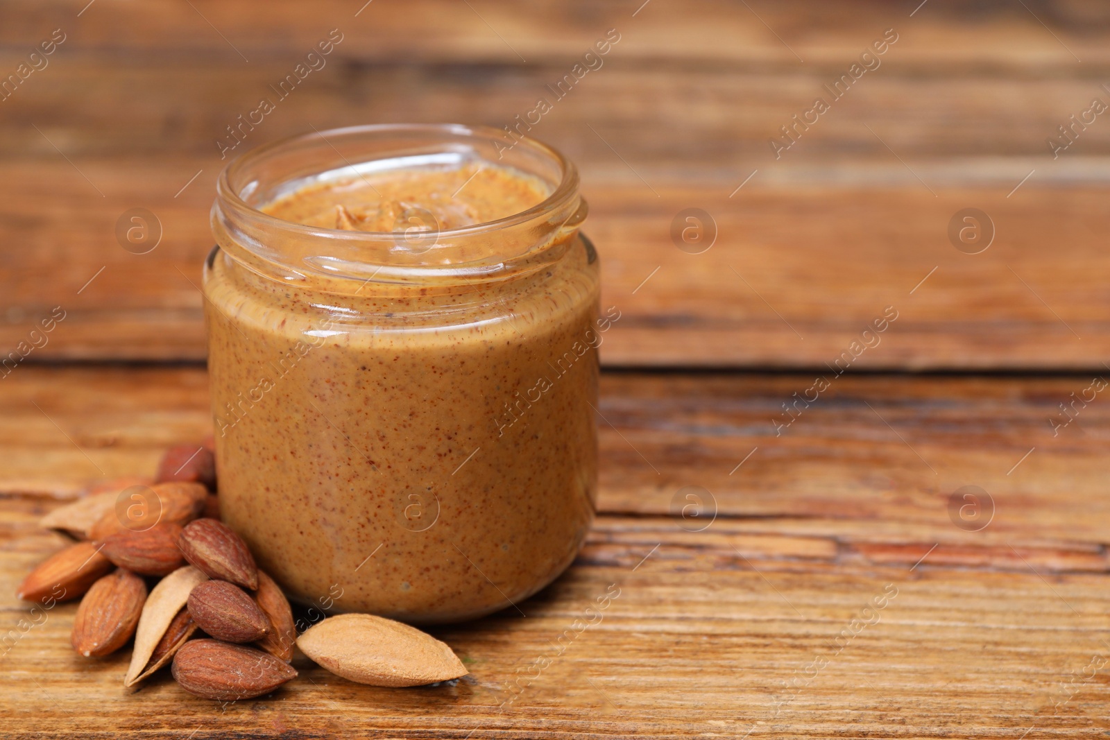 Photo of Tasty nut paste in jar and almonds on wooden table, closeup. Space for text