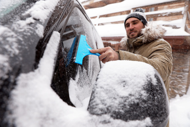 Young man cleaning snow from car window outdoors on winter day