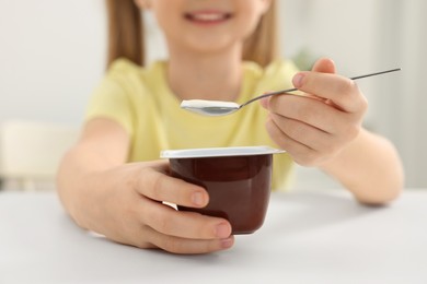 Cute little girl with tasty yogurt at white table, closeup