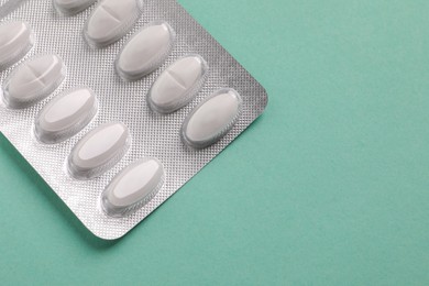 Photo of White pills in blister on pale green background, top view. Space for text