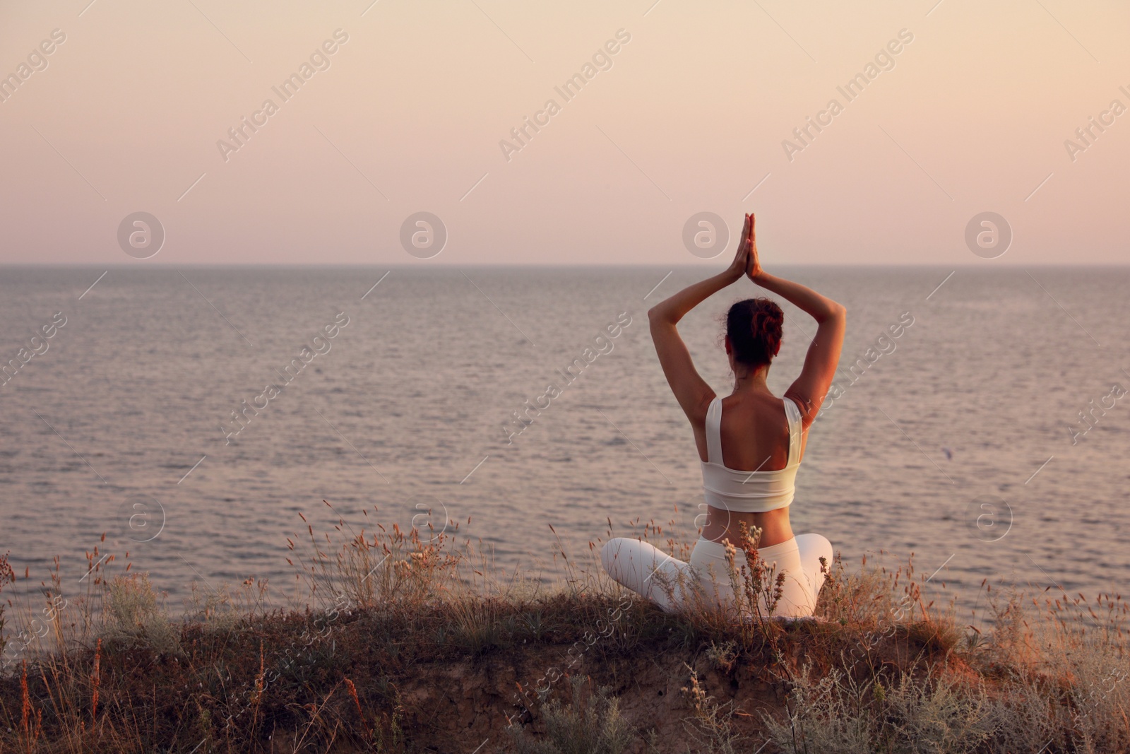 Photo of Woman meditating near sea, back view. Space for text