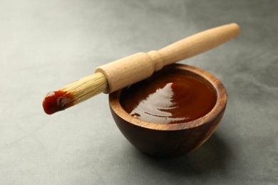 Photo of Tasty barbeque sauce in bowl and brush on grey textured table, closeup
