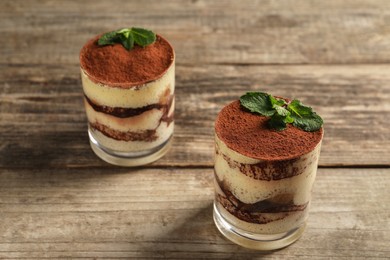 Photo of Tasty tiramisu and mint in glasses on wooden table