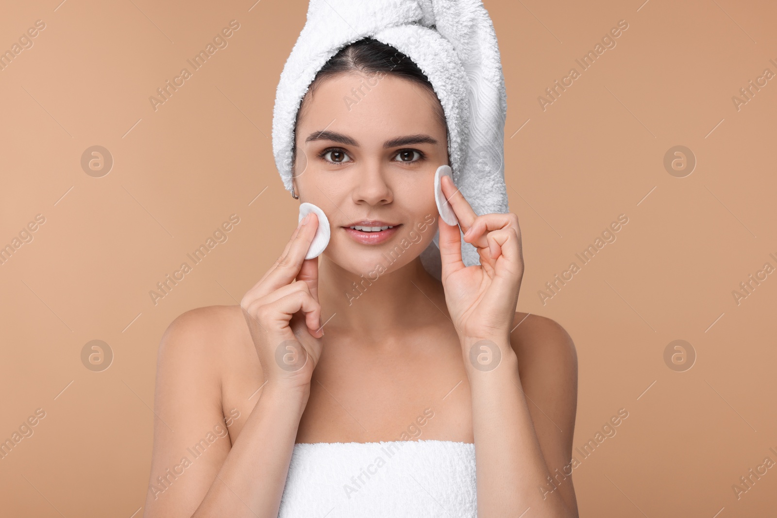 Photo of Young woman cleaning her face with cotton pads on beige background