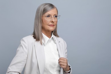Portrait of beautiful senior woman in glasses on grey background. Space for text