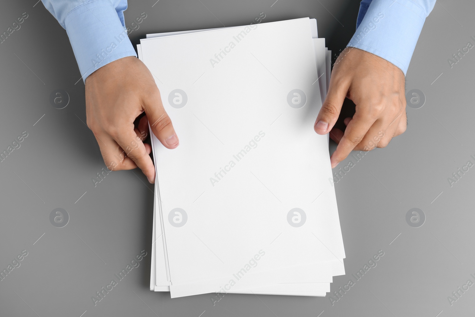 Photo of Man holding blank paper sheets for brochure at grey table, top view. Mock up