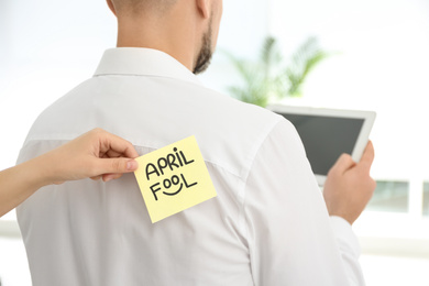 Photo of Woman sticking APRIL FOOL note to colleague's back in office, closeup
