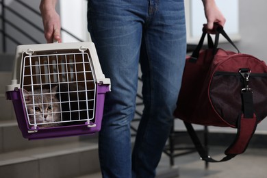 Photo of Travel with pet. Man holding carrier with cute cat and bag indoors, closeup