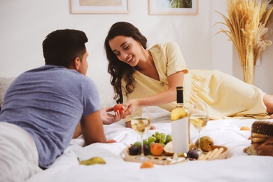 Happy couple with wine and tasty food imitating picnic at home