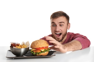 Photo of Young hungry man and plate with French fries and tasty burger on white background