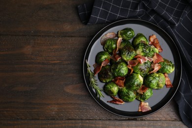 Photo of Delicious roasted Brussels sprouts and bacon on wooden table, top view. Space for text