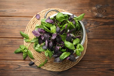 Photo of Metal colander with different fresh basil leaves on wooden table, top view