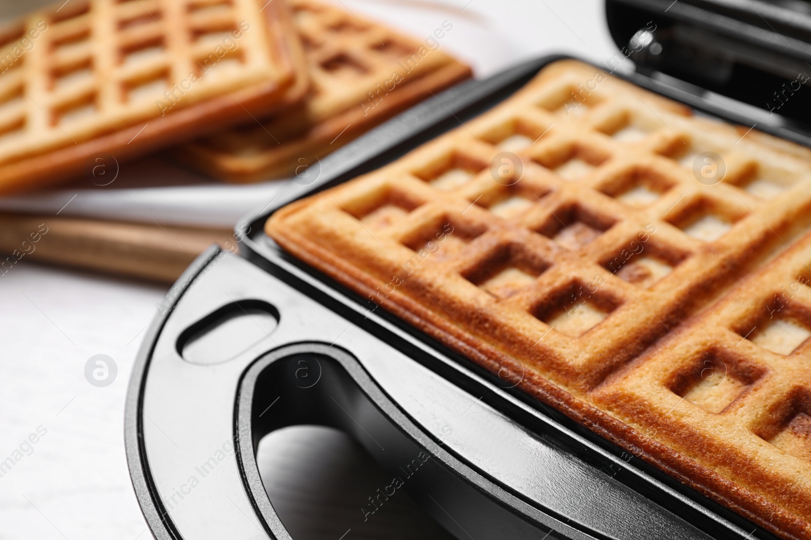 Photo of Modern iron with tasty Belgian waffles on table, closeup