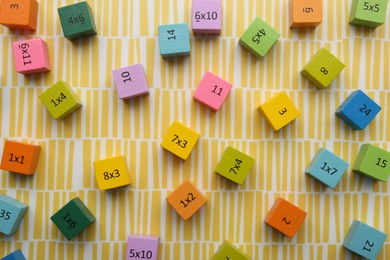 Colorful cubes with numbers and multiplications on yellow background, flat lay