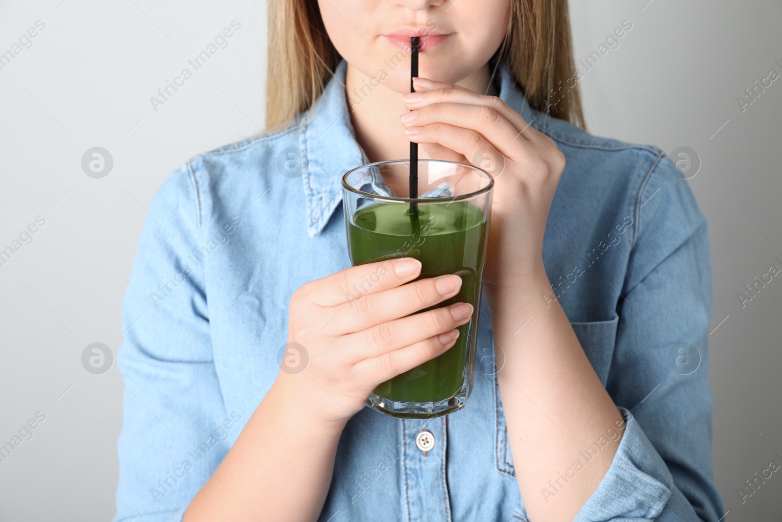 Photo of Woman drinking spirulina shake from glass on grey background, closeup