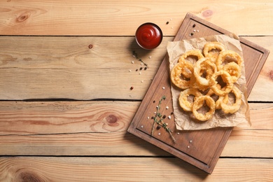 Photo of Homemade crunchy fried onion rings and tomato sauce on wooden background, top view. Space for text