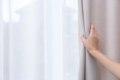 Woman opening window curtains at home, closeup. Space for text