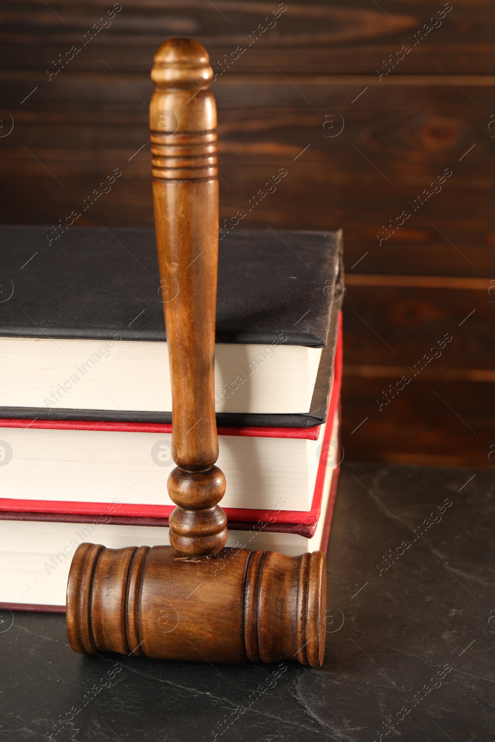 Photo of Wooden gavel and stack of books on dark textured table, closeup