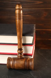 Photo of Wooden gavel and stack of books on dark textured table, closeup