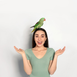 Photo of Young woman with Alexandrine parakeet on light background. Cute pet