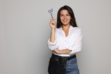 Photo of Portrait of happy hairdresser with professional scissors on light grey background