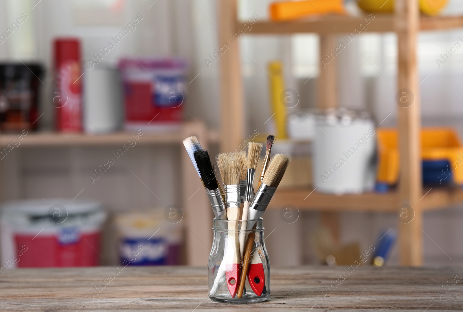 Photo of Glass jar with paint brushes on wooden table in workshop. Space for text