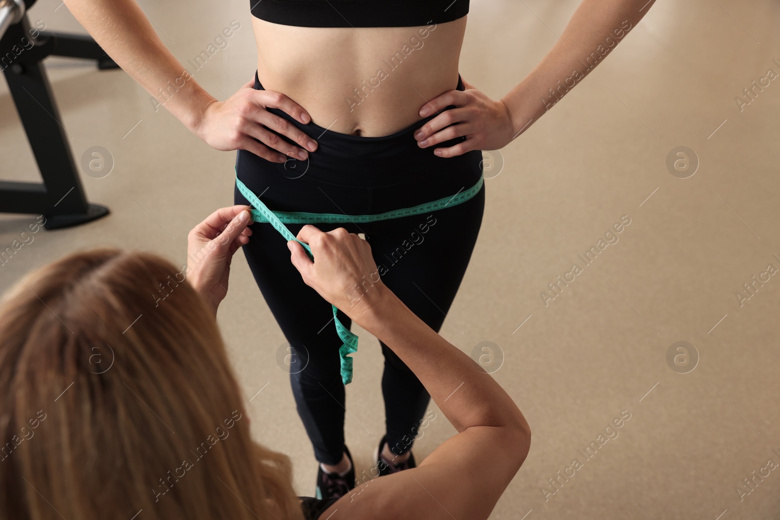 Photo of Trainer measuring woman`s hips with tape in gym, closeup