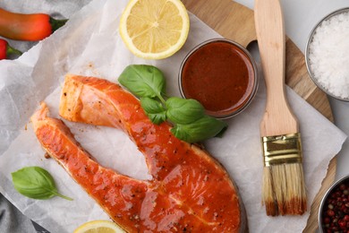 Photo of Fresh marinade, fish, lemon, brush and basil on white table, flat lay