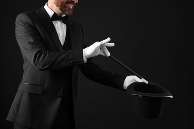 Magician showing magic trick with top hat on black background, closeup