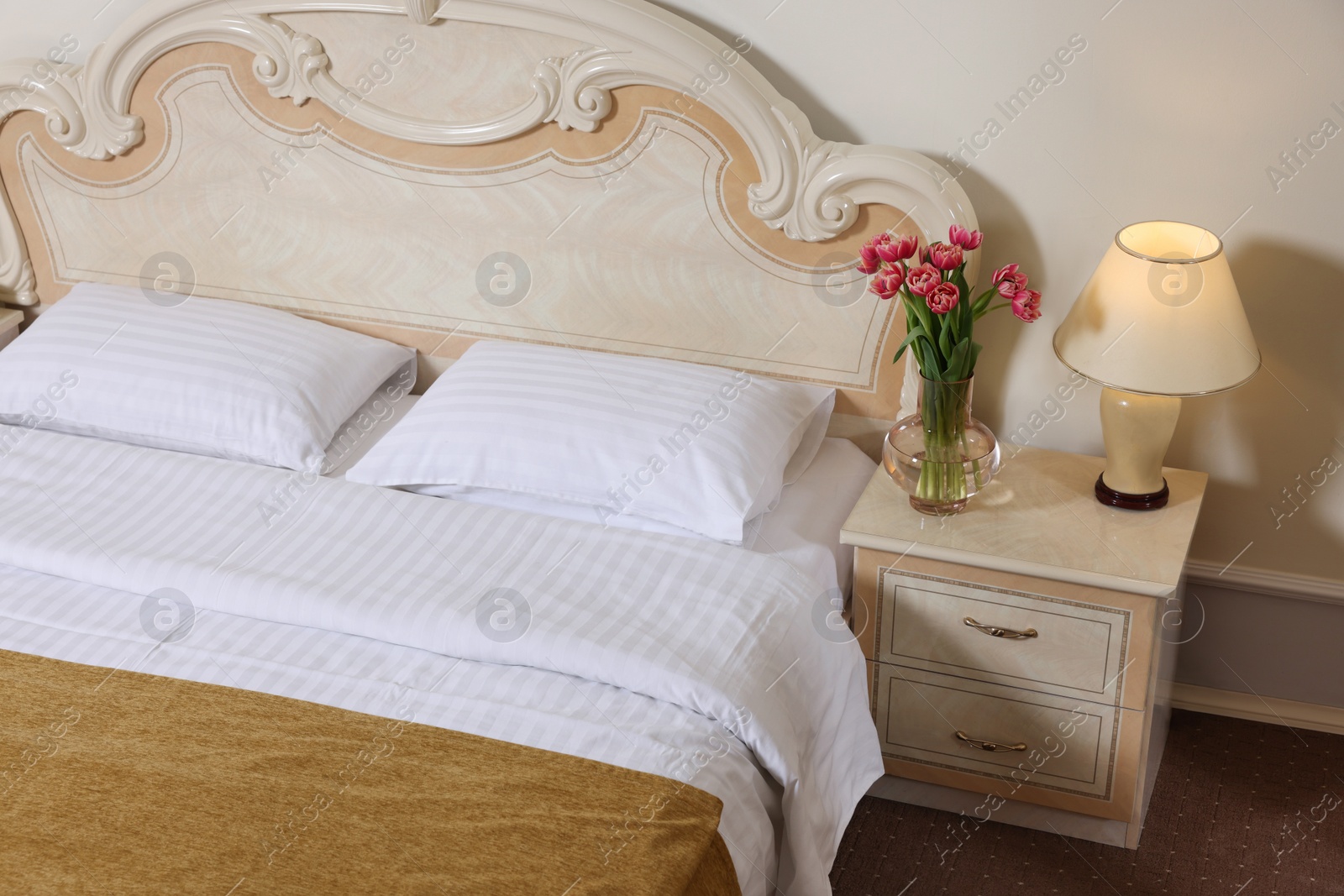 Photo of Stylish bedroom interior with comfortable bed, lamp and vase of flowers